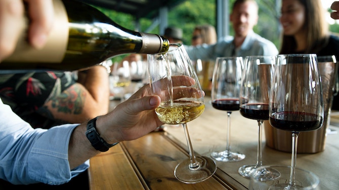 Someone pouring wine into a glass on a table with several other glasses of wine