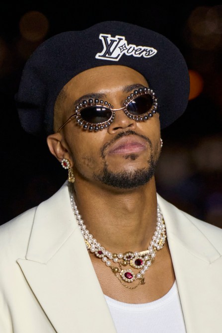 A model wearing layered pearl and jewel necklaces, jewel earrings, and embellished sunglasses
