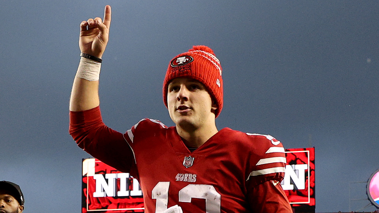 Brock Purdy Diet. Brock Purdy in a red beanie and jersey holding up his hand with his pointer finger.