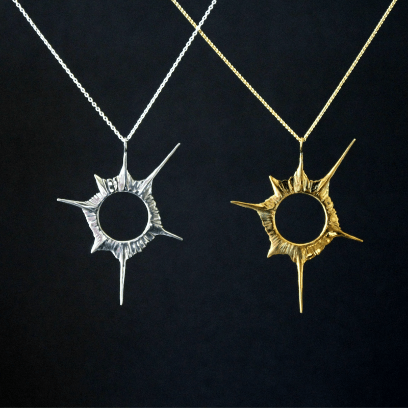 Two solar eclipse pendant necklaces, one silver and one gold