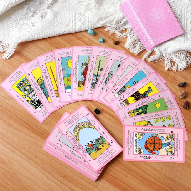 A deck of pink tarot cards laid out on the floor, near a blanket, a journal, and crystals