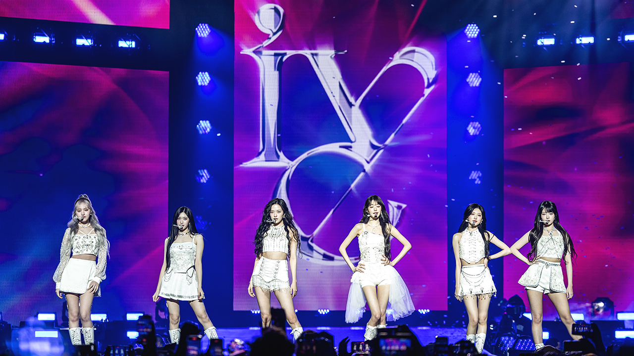 K-Pop Girl Group IVE, six Asian women ANYUJIN, GAEUL, REI, JANGWONYOUNG, LIZ, and LEESEO, standing with white outfits on stage.