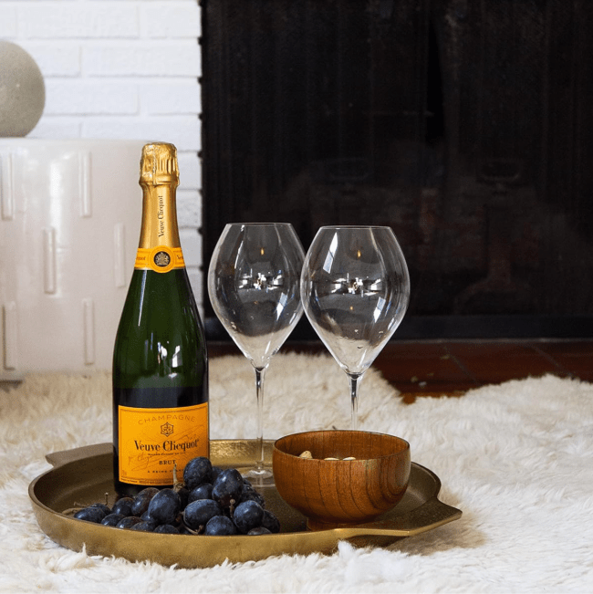 A tray topped with Veuve Cliquot champagne, two glasses, grapes, and a wooden bowl