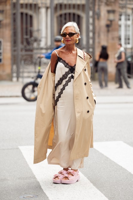 Grece Ghanem wears pink Chanel sandals, white and black silk dress, beige trench coat and sunglasses outside the Gestuz show during day four of the Copenhagen Fashion Week (CPHFW) SS25 on August 08, 2024 in Copenhagen, Denmark.
