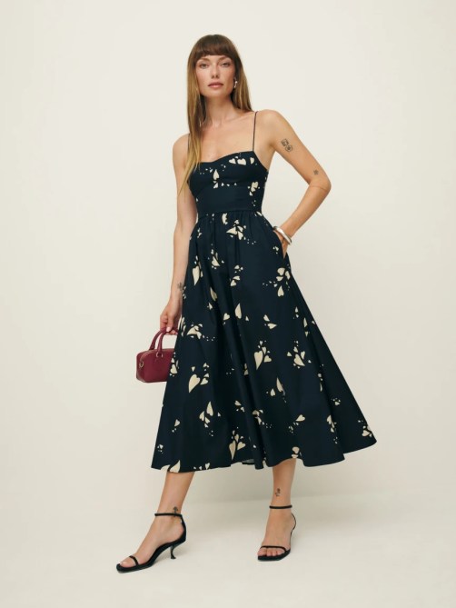 A woman wearing a black dress with black strappy heels and a red handbag