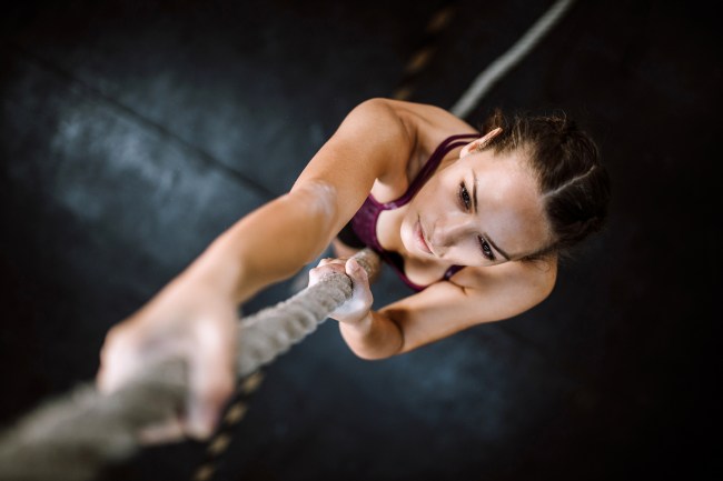 Young woman climbing rope in gym