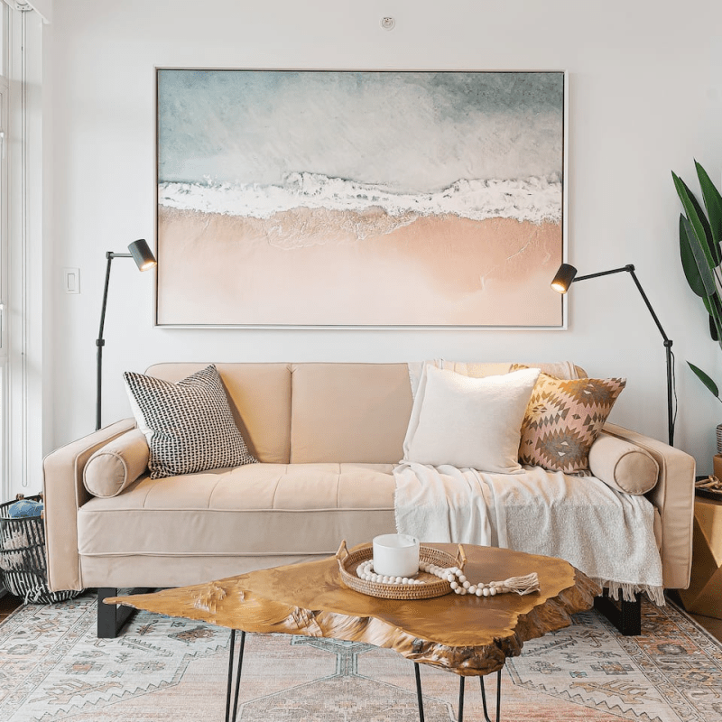 A living room with a couch, a coffee table, a painting on the wall, two floor lamps, a plant, a side table, and more. A Yaletown, Vancouver Airbnb.