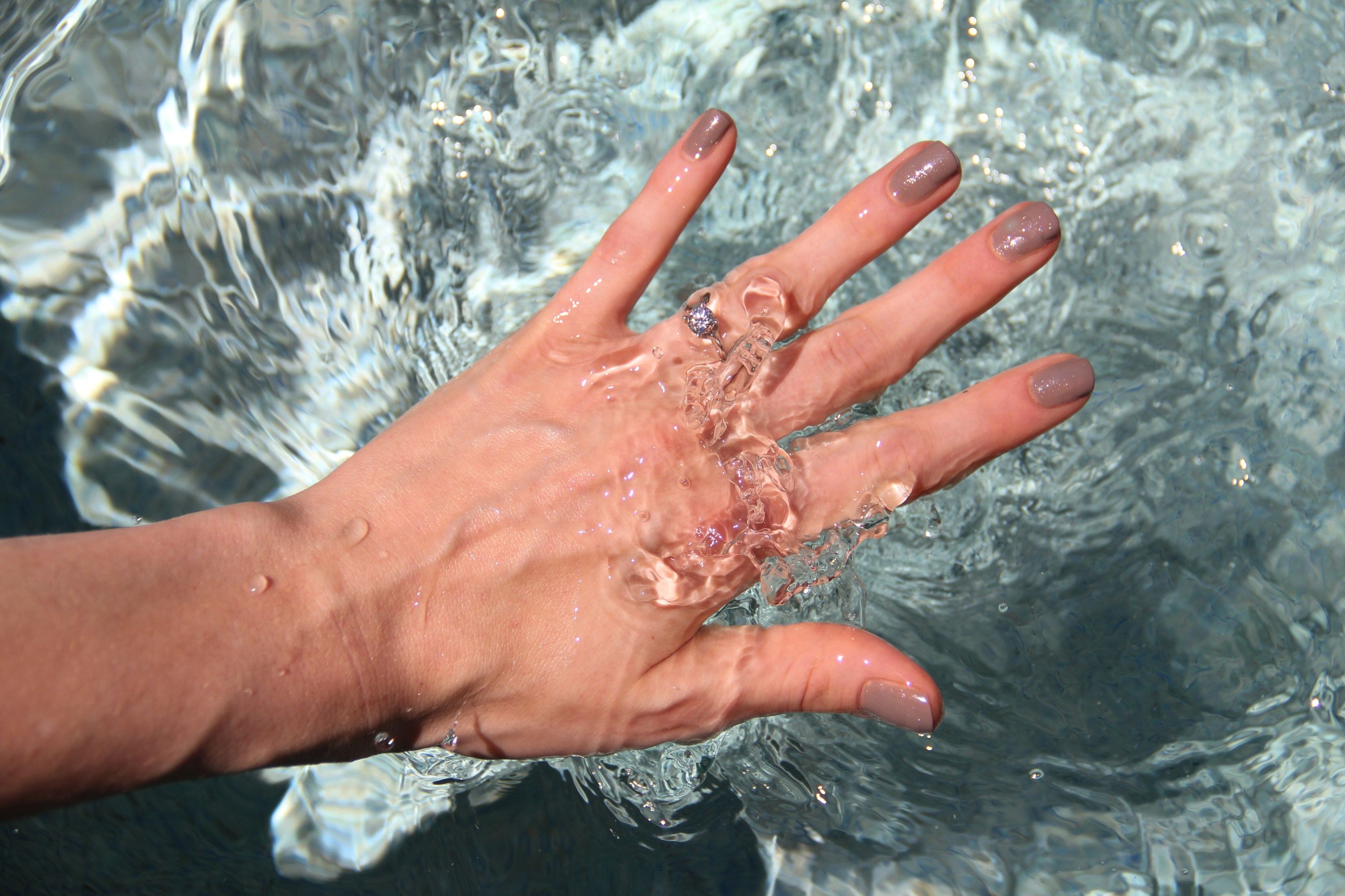 Surface level view of woman's hand plunging in water.