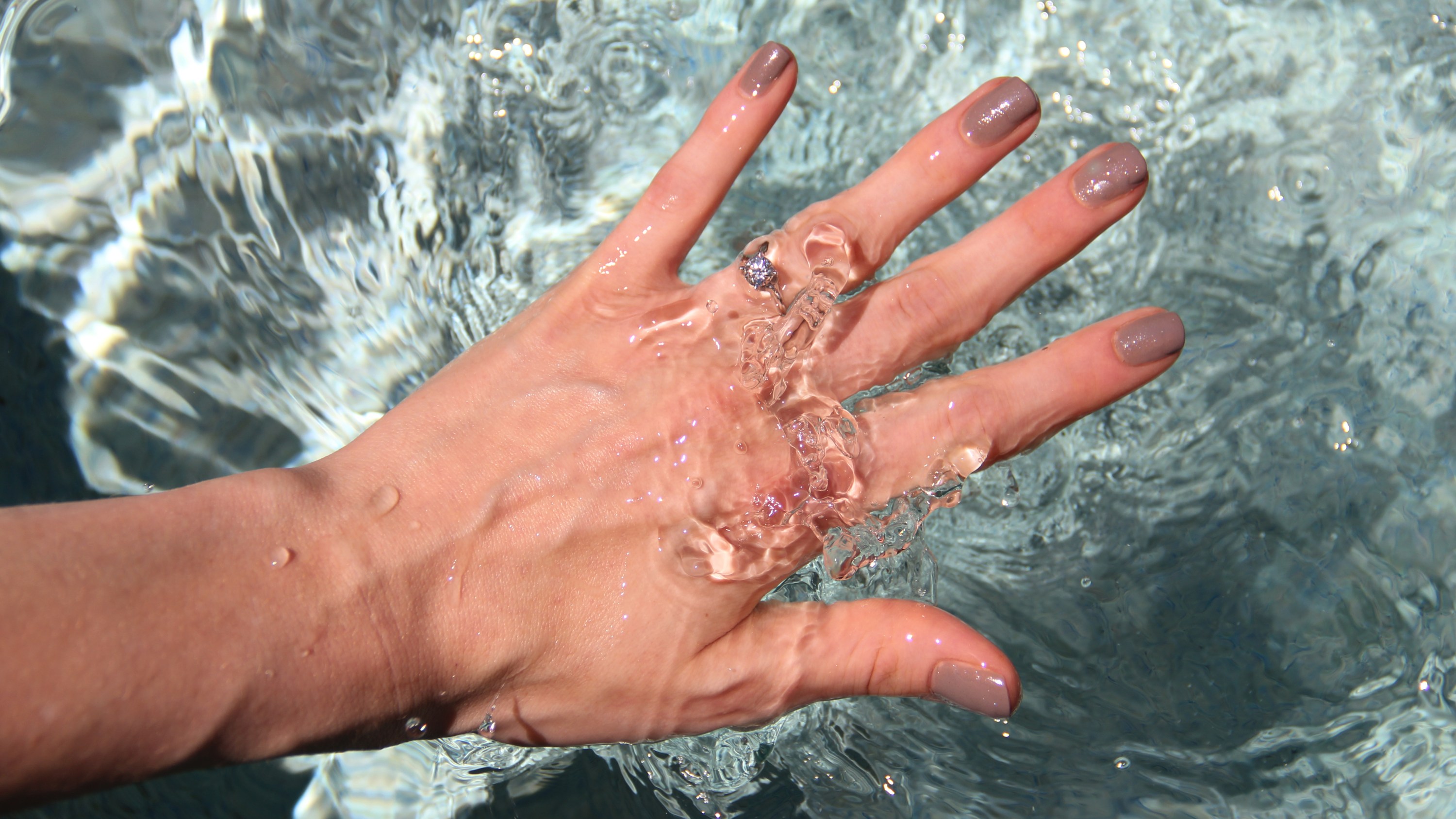 Surface level view of woman's hand plunging in water.