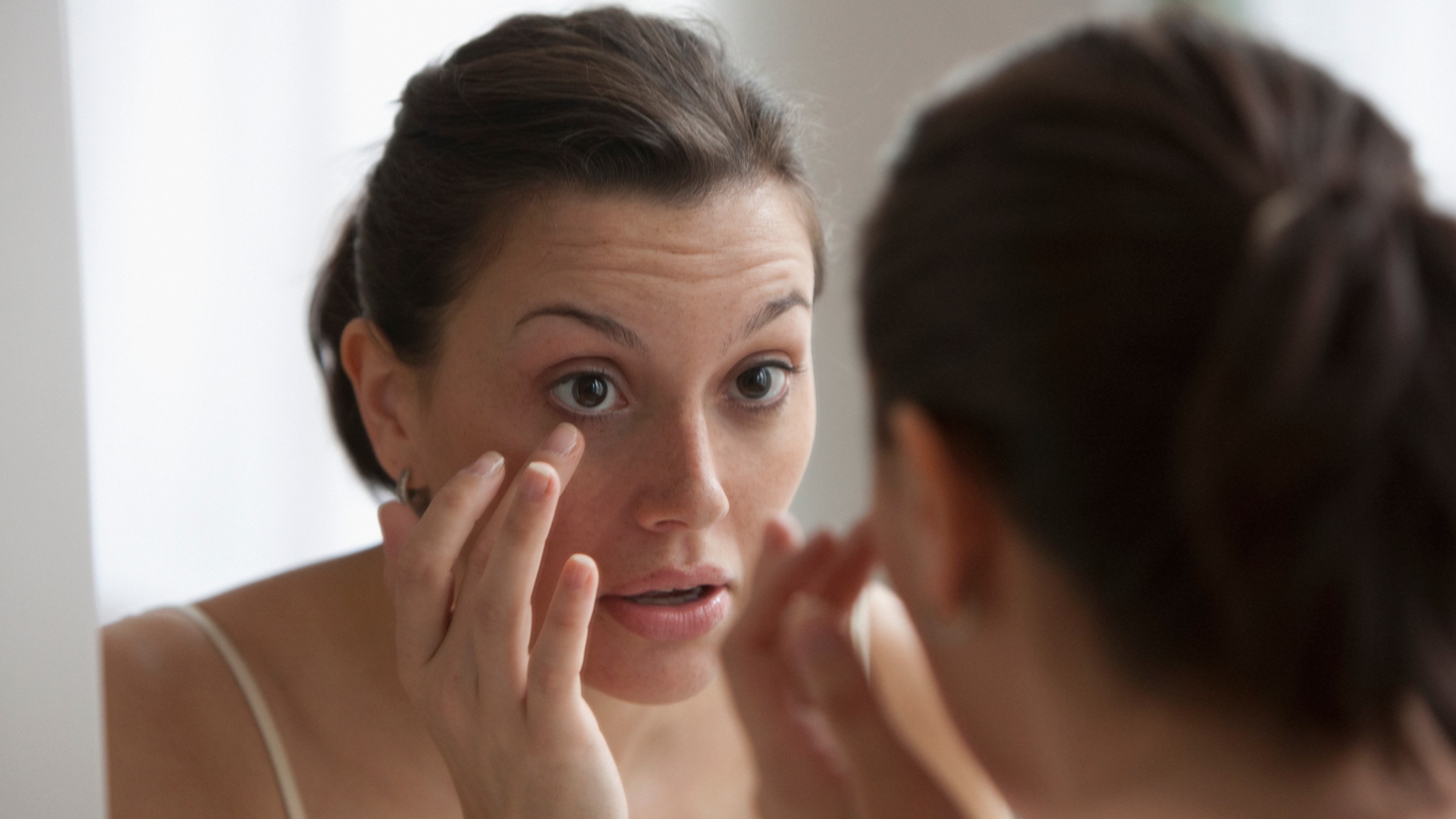 Young woman checking her eye in the mirror
