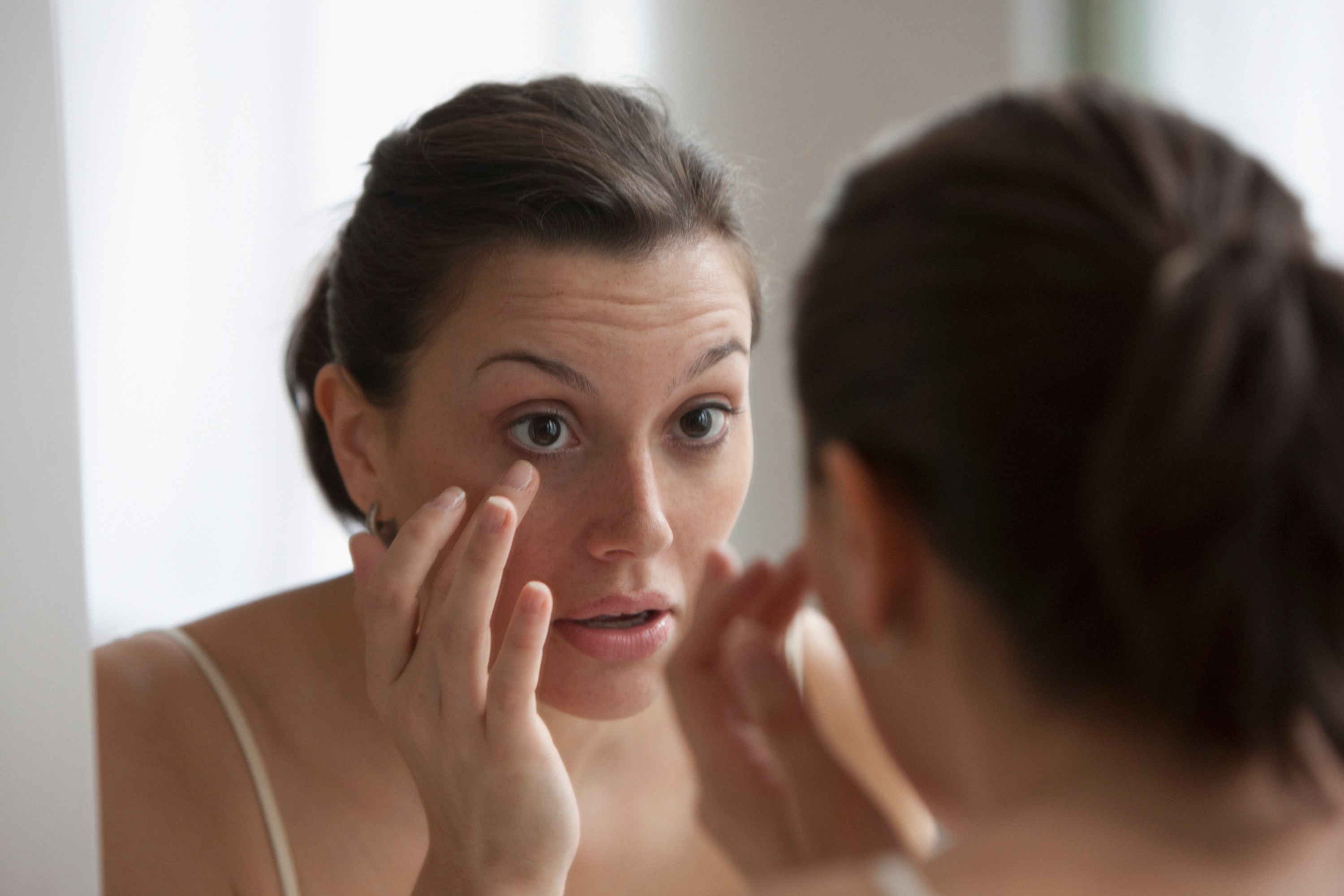 Young woman checking her eye in the mirror