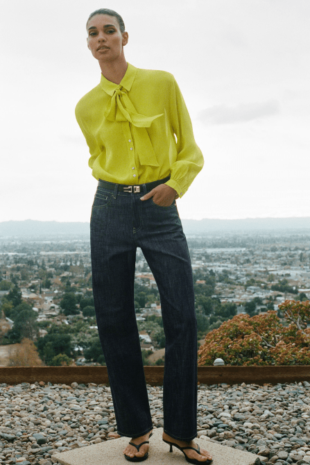 A model wearing the Zara High Waisted Straight Leg Slim Fit Belted Jeans in a dark wash with a bright green blouse and heeled thong sandals
