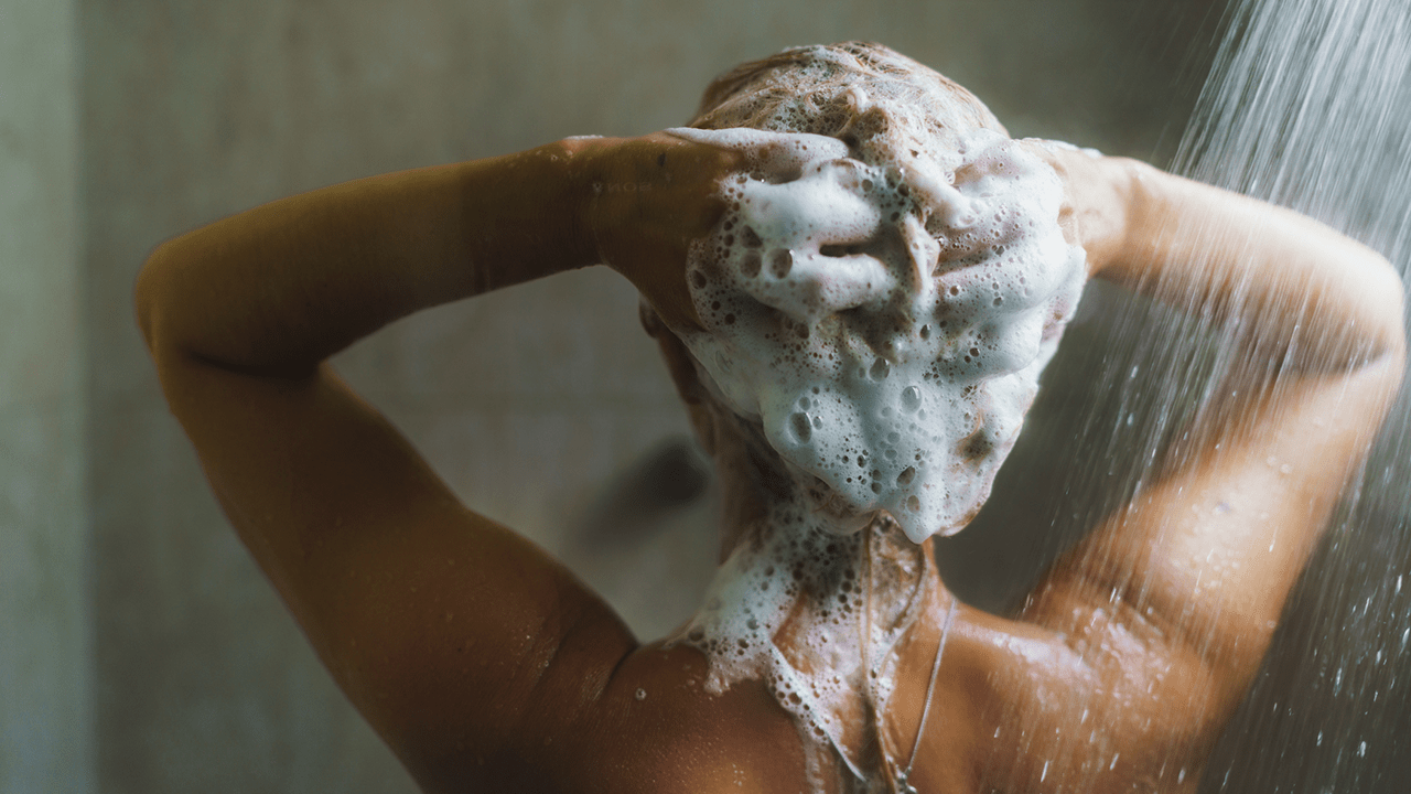 Woman washing her hair with shampoo and foam, water splashing in the shower.