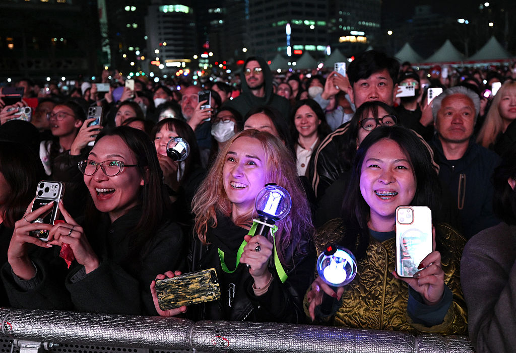 BTS fans react as they watch the comeback concert of K-pop boy group BTS on a screen at the venue in Seoul on March 21, 2026. South Korean megastars BTS reunited on March 21 for their first show in nearly four years, blowing away enormous crowds in Seoul for a K-pop extravaganza livestreamed to millions more worldwide. (Photo by Jung Yeon-je / AFP via Getty Images).